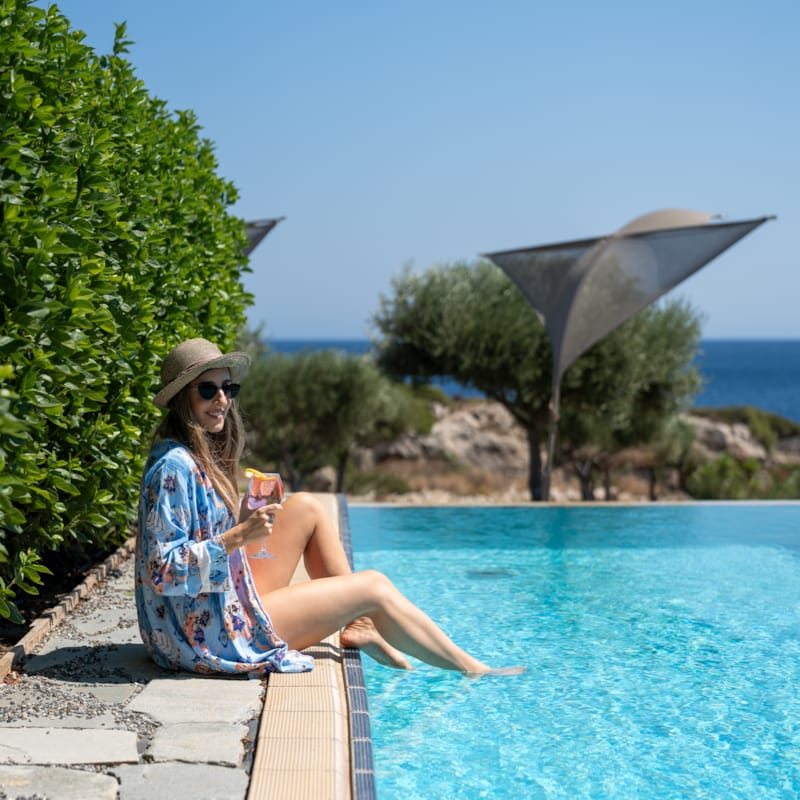 a person sitting on a stone ledge by a pool with an umbrella